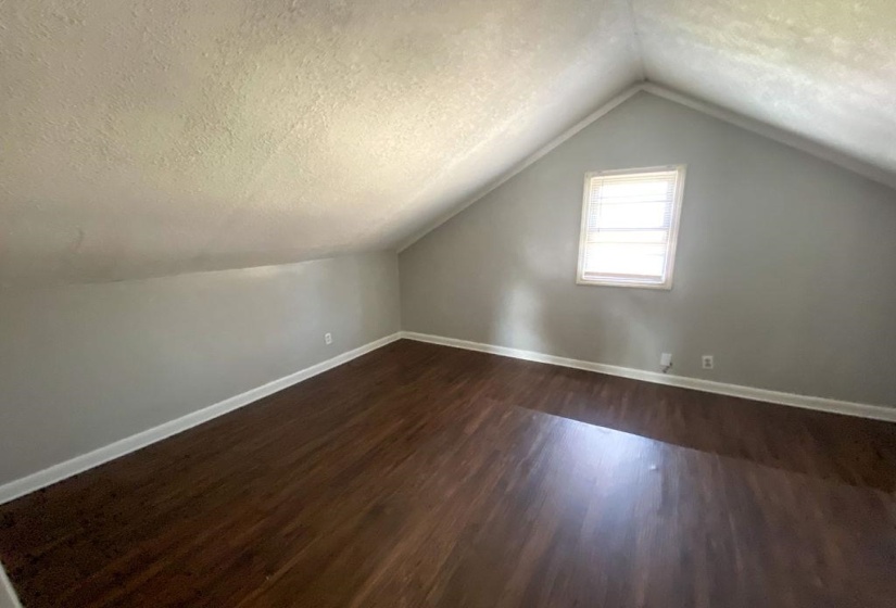 Room featuring sloped ceilings, light gray wall paint, dark wood-finish flooring, white baseboards, and a window with blinds