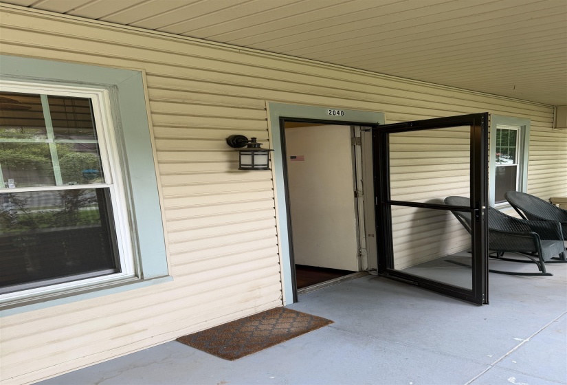 Covered porch entry featuring a storm door, an exterior wall lantern, horizontal siding, and a window with light blue trim