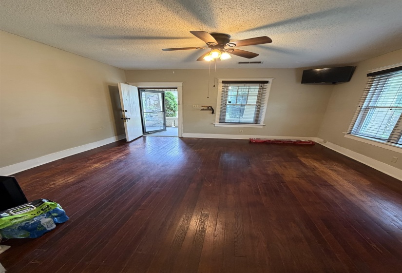 Spacious room featuring rich wood-finish flooring, a ceiling fan with integrated lighting, and multiple windows with horizontal blinds