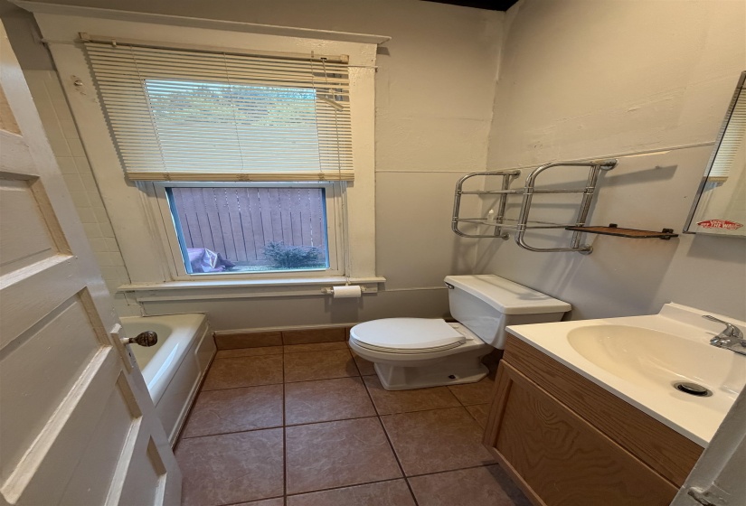 Bathroom featuring a window with blinds, a white bathtub, a toilet, a vanity with an integrated sink, and tile flooring