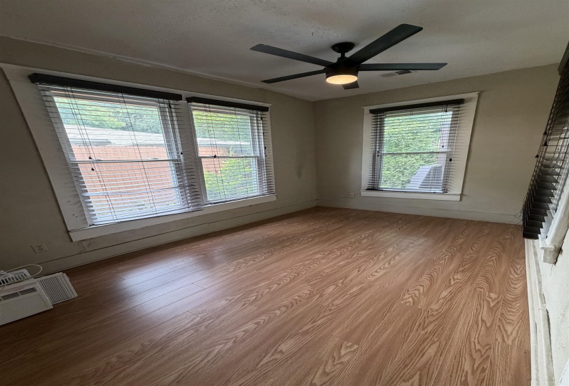 Spacious room featuring wood-finish flooring, multiple windows, a modern ceiling fan with integrated lighting, and neutral wall tones