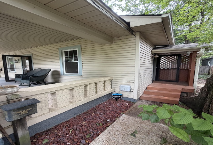 Front exterior featuring horizontal siding, a covered porch with a brick half-wall, wood-finish steps, and a lattice screen door