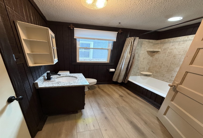 Bathroom featuring a full tub and shower with tiled surround, wood-finish flooring, a vanity with granite-style countertop, and wall-mounted shelving
