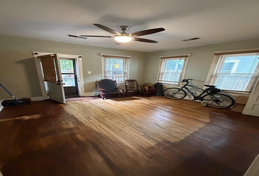 Hardwood flooring with a partially stained finish, three windows with blinds, and a ceiling fan with integrated lighting