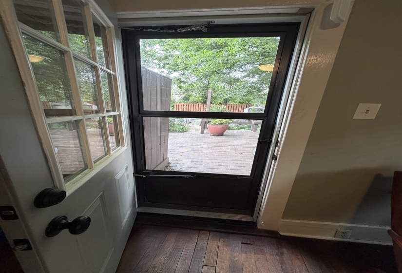 Wood-finish flooring with a white paneled door and a screen door leading to an outdoor deck