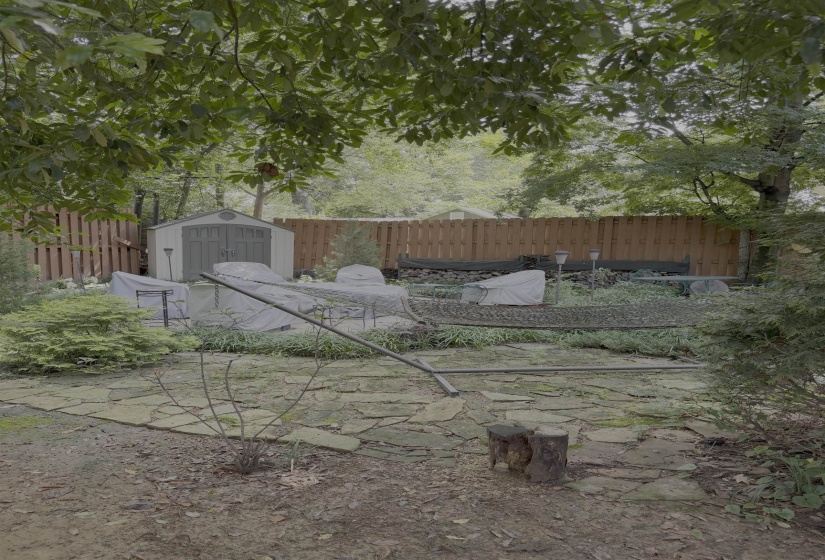Expansive backyard featuring flagstone patio, mature trees, privacy fencing, and a storage shed