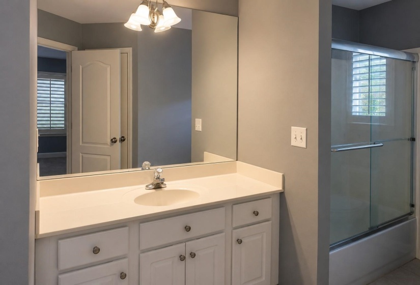 Bathroom vanity featuring a single basin sink, white cabinetry with round hardware, and a large mirror