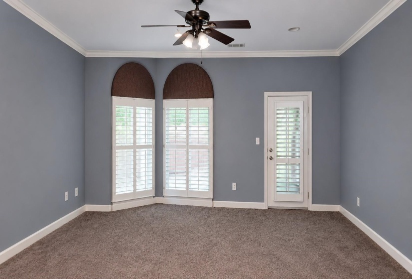 Room featuring arched windows with plantation shutters, a glass-paneled door, crown molding, and a ceiling fan with integrated lighting