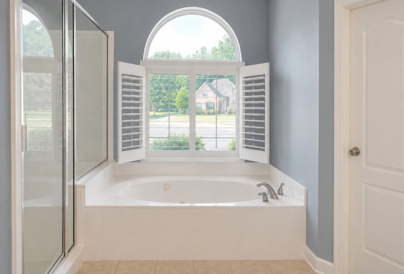 Soaking tub with a large arched window, white plantation shutters, and a brushed nickel faucet