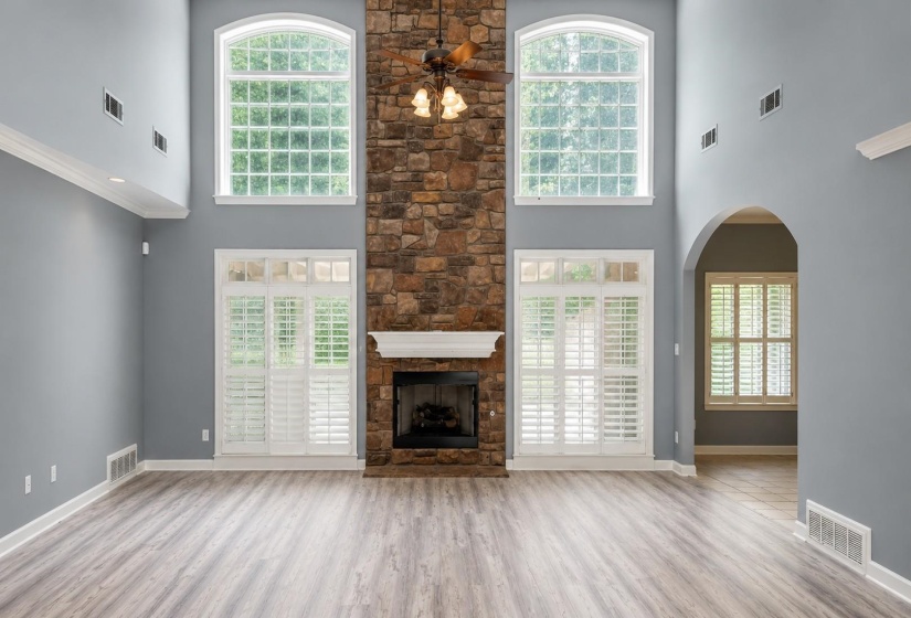 Spacious living area featuring a floor-to-ceiling stone fireplace with a white mantel, wood-finish flooring, and high ceilings