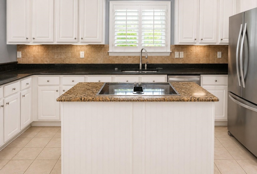 Kitchen featuring white cabinetry, dark countertops, a central island with a cooktop, stone tile backsplash, and stainless steel appliances