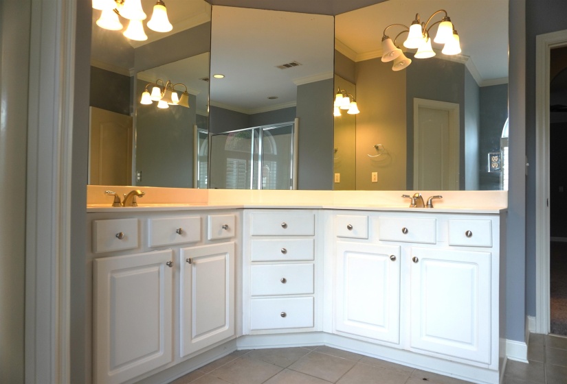 Dual vanity featuring white cabinetry with brushed nickel hardware, light-toned countertops, and multiple mirrored panels