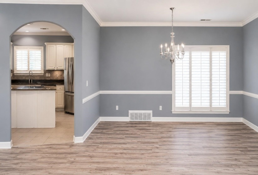 Spacious room featuring wood-finish flooring, a crystal chandelier, and a large window with white plantation shutters