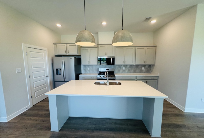 Kitchen featuring stainless steel appliances, tasteful backsplash, an island with sink, hanging light fixtures, and light countertops