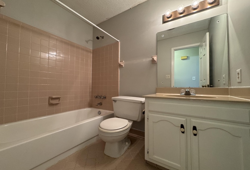 Bathroom featuring a white bathtub, beige tiled shower surround, toilet, and a vanity with white cabinetry, a built-in sink, and an overhead light fixture