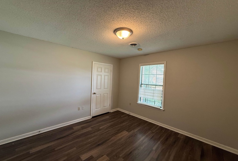 Neutral-toned interior room with wood-finish flooring, a paneled door, and a single window with grids