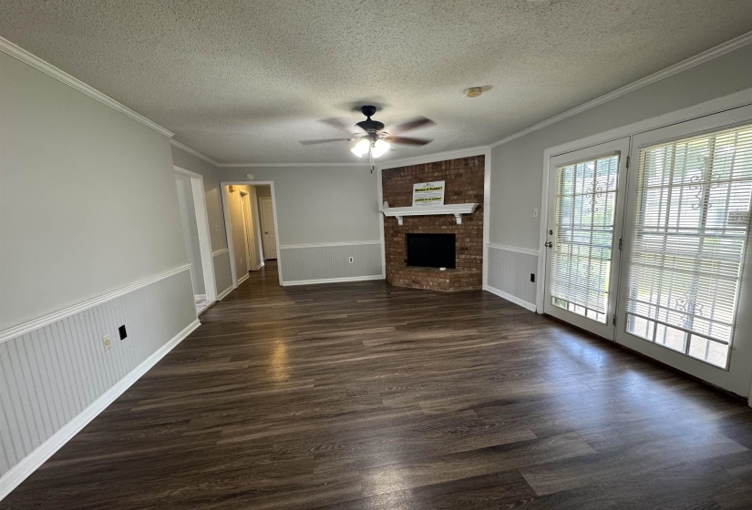 Spacious room featuring wood-finish flooring, a brick fireplace with a white mantel, and ceiling fan