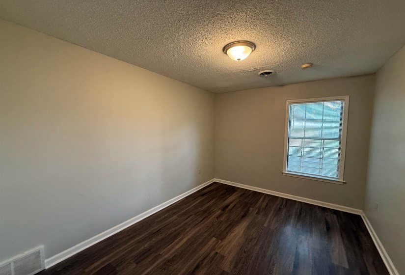 Room featuring wood-finish flooring, white baseboards, a single window, and a flush-mount ceiling light fixture