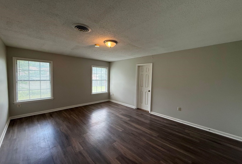 Spacious interior featuring wood-finish flooring, two large windows, neutral wall tones, and a paneled door