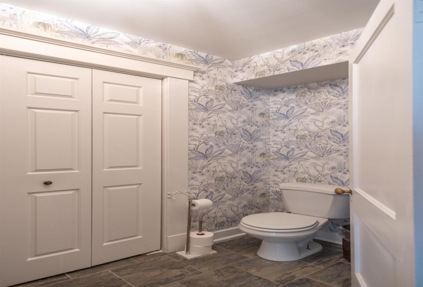 Powder room featuring botanical wallpaper, a white toilet, and dark tile flooring