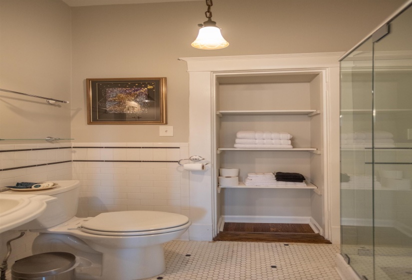 Bathroom featuring white subway tile wainscoting, built-in shelving, glass-enclosed shower, pedestal sink, and hexagonal tile flooring