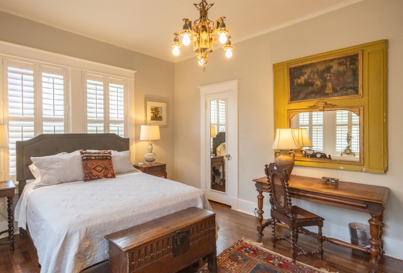 Bedroom featuring rich wood-finish flooring, a decorative chandelier, and white plantation shutters on the windows