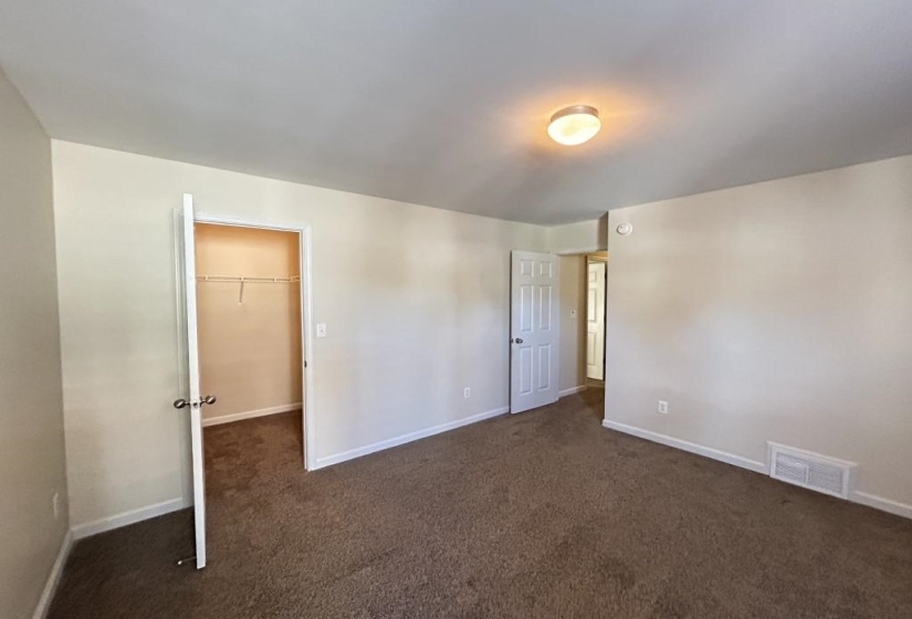 Unfurnished bedroom featuring a closet, dark colored carpet, and a walk in closet