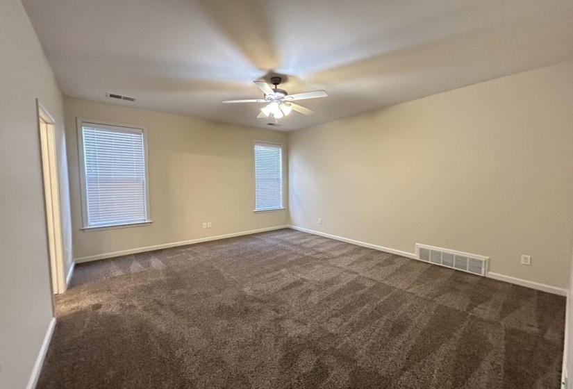 Empty room featuring ceiling fan, dark colored carpet, and a wealth of natural light