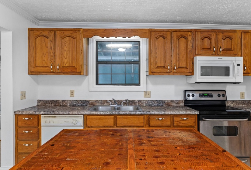 Kitchen featuring wood cabinetry, laminate countertops, a stainless steel electric range, an over-the-range microwave, and a double basin sink