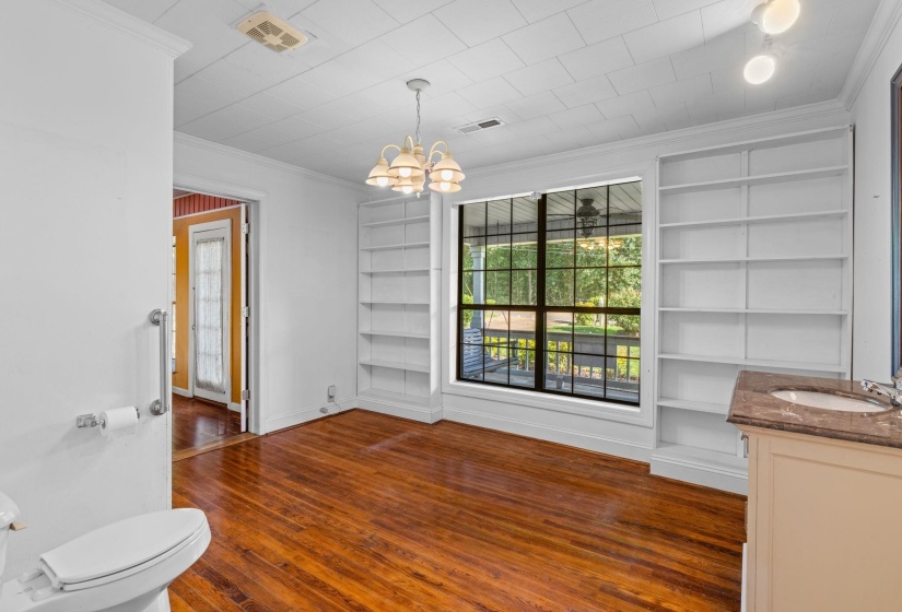 Room featuring a large window, built-in shelving, rich wood-finish flooring, and a vanity with a countertop and undermount sink