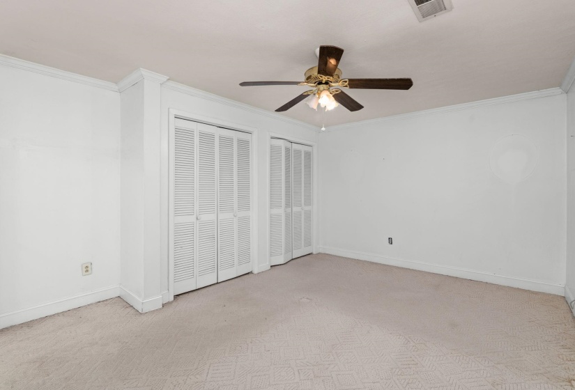 Spacious room featuring a ceiling fan with light fixture, dual bi-fold louvered closet doors, and crown molding