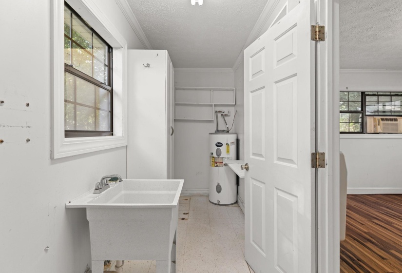 Utility room with a deep basin sink, window, built-in shelving, and a water heater
