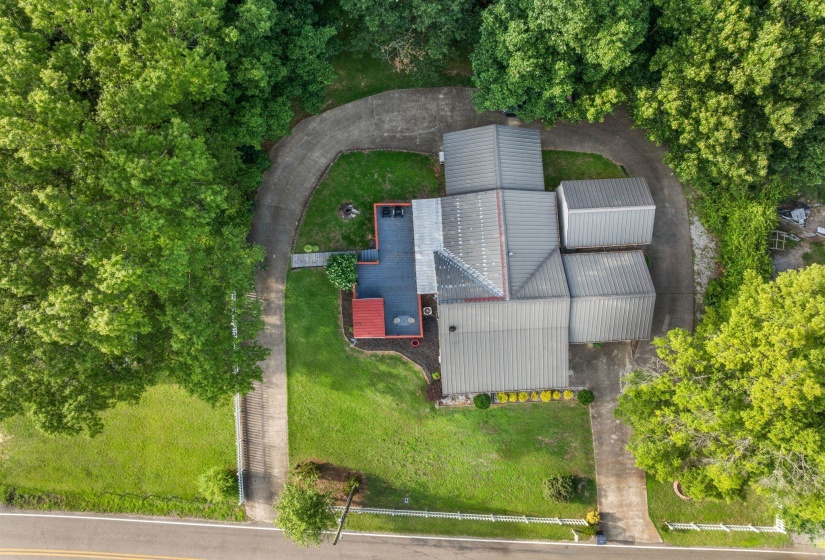 Property featuring a metal roof structure, expansive paved driveway, and manicured landscaping