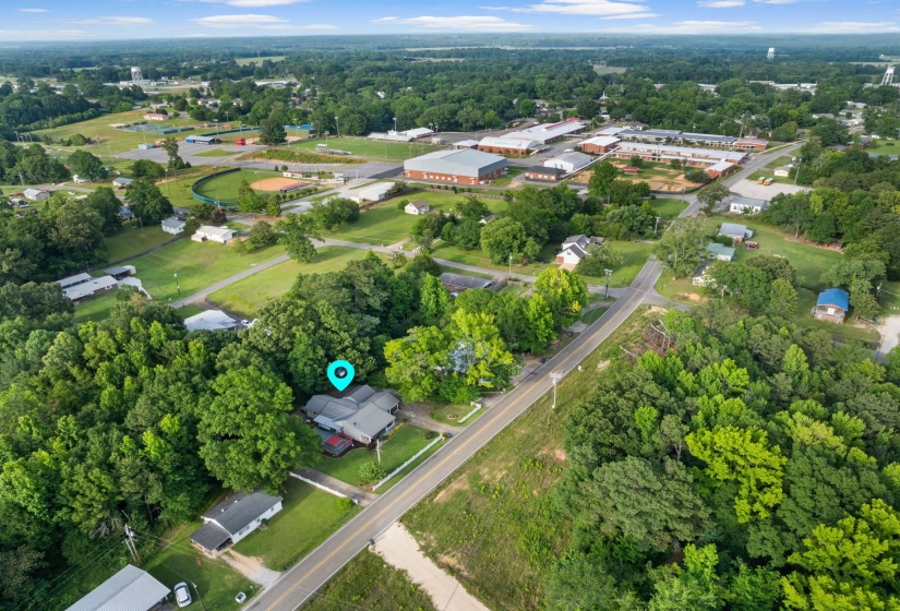 Aerial perspective showcasing the property surrounded by mature trees, a paved road, and verdant landscaping