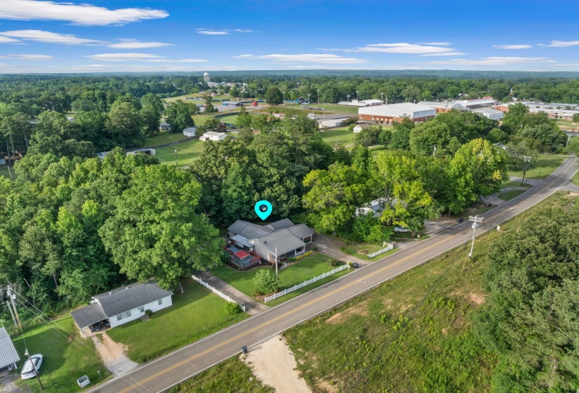 Aerial perspective featuring a residential property with surrounding mature trees, a white picket fence, and a paved driveway