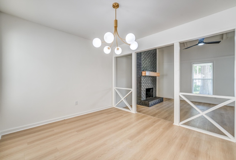 Open-concept living space featuring wood-finish flooring, a modern brass chandelier, and a black brick fireplace with a wood mantle