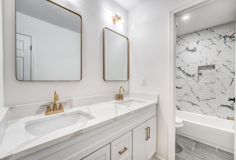 Double vanity with integrated sinks, white cabinetry, gold-finish hardware, and marble-look countertop