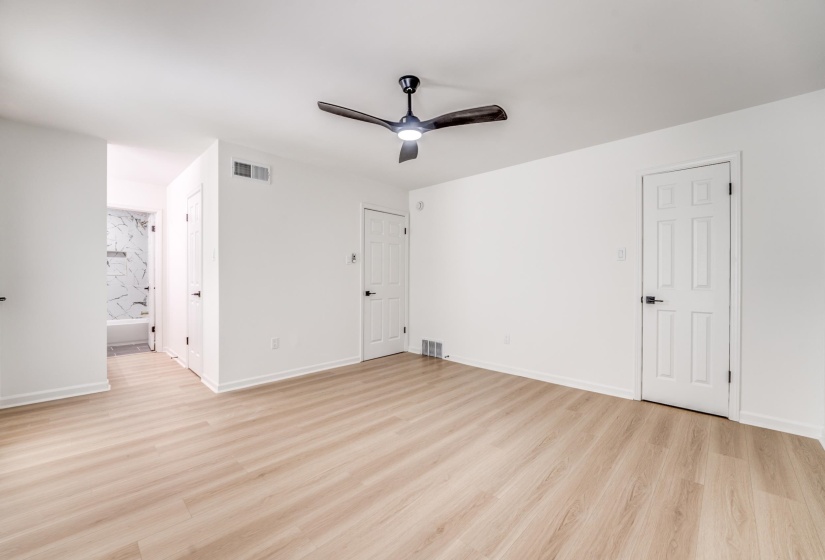 Spacious room featuring light wood-finish flooring, a modern black ceiling fan, white paneled doors with matte black hardware, and crisp white walls