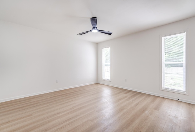 Spacious interior room featuring light wood-finish flooring, white walls, and a contemporary ceiling fan with integrated lighting