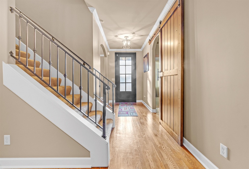 Entryway featuring wood-finish flooring, a barn door, and an arched hallway leading to a glass-paneled door