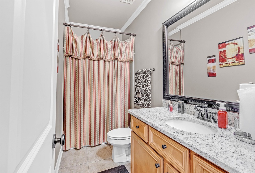 Bathroom featuring a wood-finish vanity with an undermount sink, a granite-style countertop, and a framed mirror