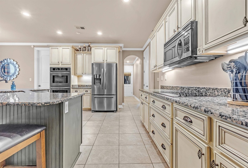 Kitchen featuring extensive cabinetry with decorative hardware, stone countertops, stainless steel appliances, and tile flooring