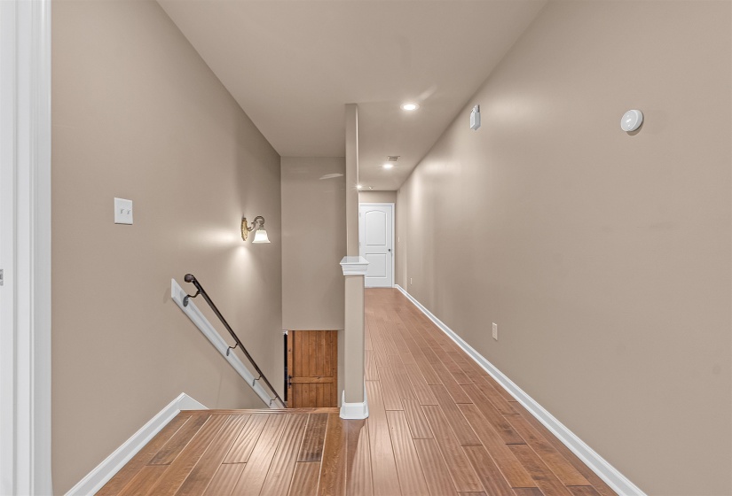 Hallway featuring wood-finish flooring, recessed lighting, and a staircase with a black metal handrail