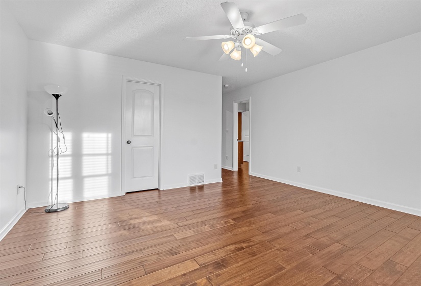 Spacious room featuring wood-finish flooring, crisp white walls, a ceiling fan with integrated lighting, and a white interior door