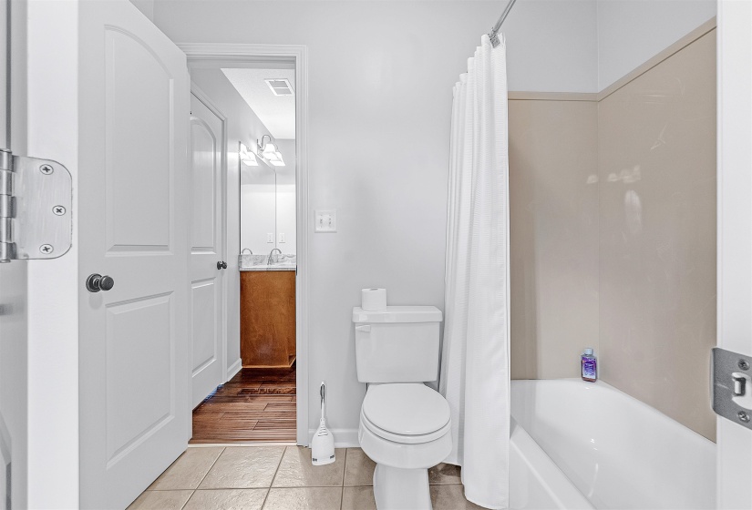 Full bathroom with a white tub and shower surround, light-toned floor tiling, and a white toilet