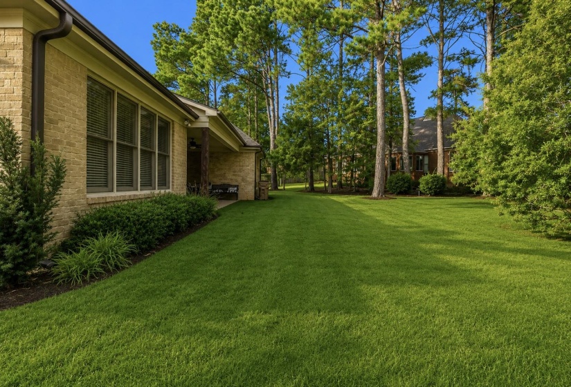 Expansive green lawn bordering a brick exterior residence with a covered patio