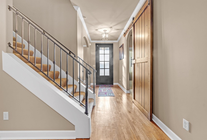 Entryway featuring wood-finish flooring, a barn door, a staircase with wrought iron balusters, a paneled glass front door, and crown molding