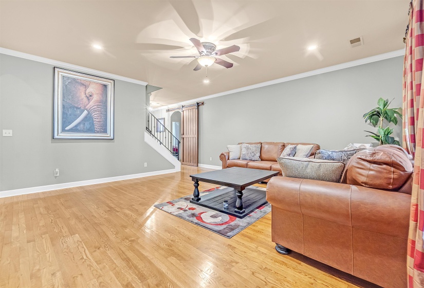 Spacious living area featuring wood-finish flooring, light gray wall paint, white crown molding, recessed lighting, and a ceiling fan