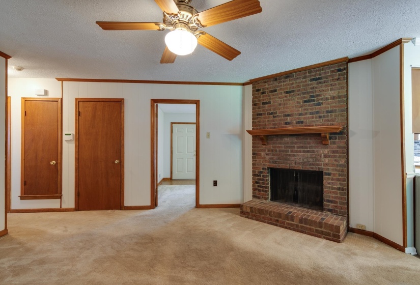 Living area featuring a brick fireplace with a wood mantel, ceiling fan with light fixture, carpet flooring, and wood trim