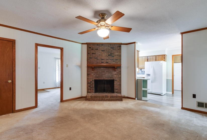 Brick fireplace with wood mantel, ceiling fan with integrated lighting, wood-finish trim, and carpeted flooring